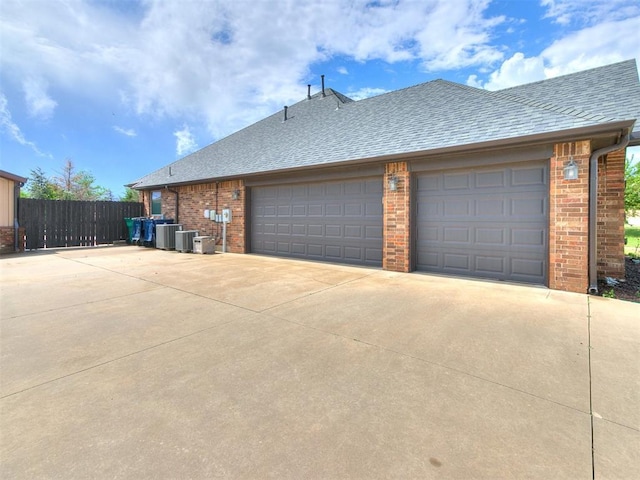 view of side of home featuring concrete driveway, fence, roof with shingles, and brick siding