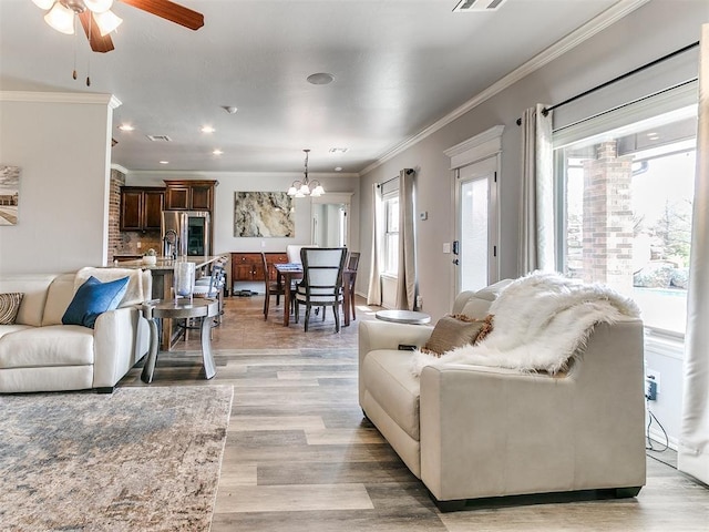 living area with recessed lighting, light wood-style floors, ornamental molding, ceiling fan with notable chandelier, and visible vents