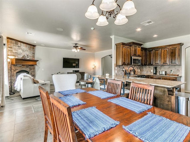 dining area featuring crown molding, visible vents, recessed lighting, a brick fireplace, and ceiling fan with notable chandelier