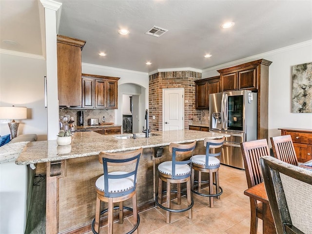 kitchen featuring a sink, decorative backsplash, crown molding, arched walkways, and stainless steel fridge with ice dispenser