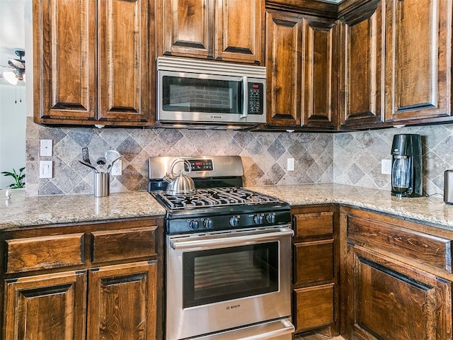 kitchen with light stone countertops, stainless steel appliances, and backsplash