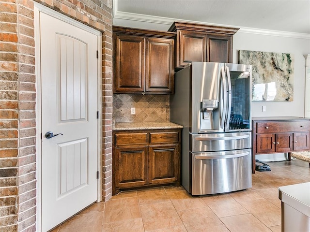 kitchen with light tile patterned floors, crown molding, brick wall, stainless steel refrigerator with ice dispenser, and backsplash