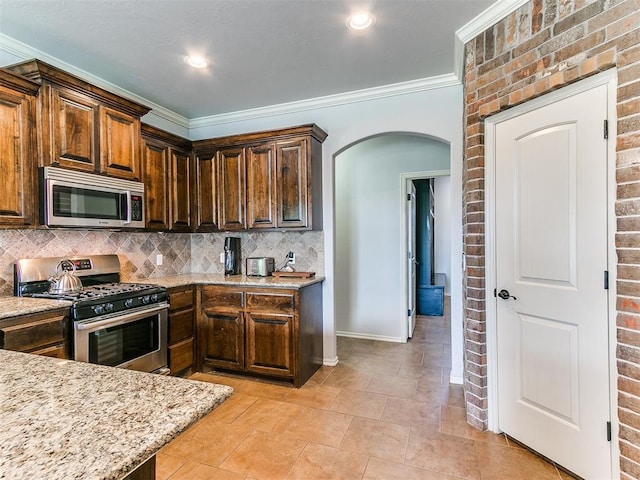 kitchen featuring light stone countertops, backsplash, ornamental molding, arched walkways, and appliances with stainless steel finishes