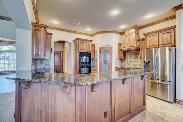 11016 Katie Beth Ln, Oklahoma City, OK 73170 - kitchen featuring stainless steel fridge, a peninsula, custom exhaust hood, arched walkways, and a breakfast bar area