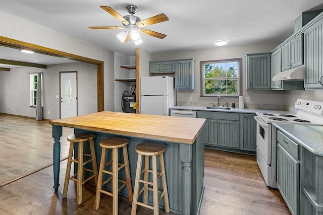 kitchen with butcher block countertops, light wood-type flooring, white appliances, under cabinet range hood, and a sink