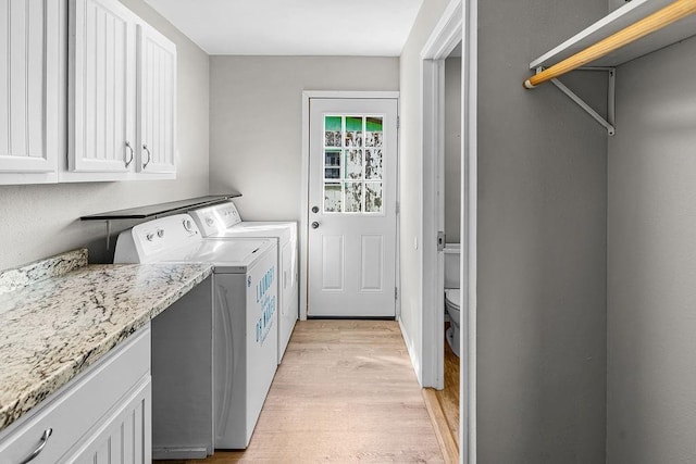 clothes washing area featuring independent washer and dryer, light wood finished floors, and cabinet space