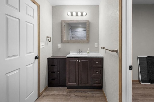 bathroom with vanity, visible vents, wood finished floors, a textured wall, and baseboards