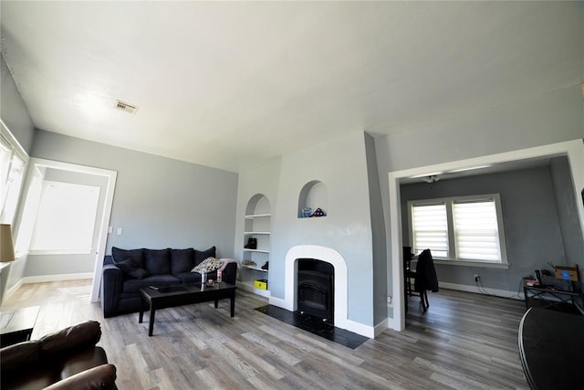 living area with visible vents, a fireplace with flush hearth, wood finished floors, built in shelves, and baseboards