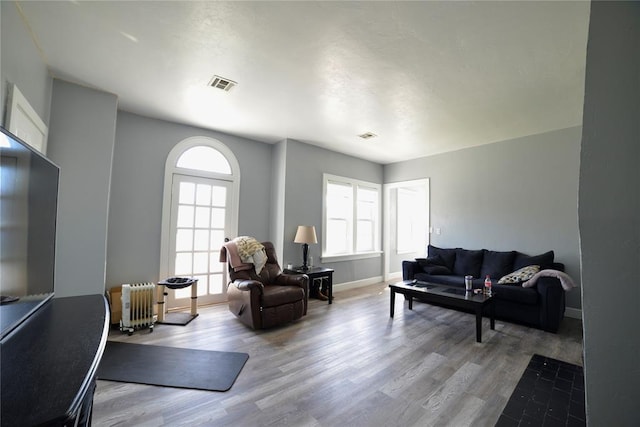 living area featuring baseboards, visible vents, wood finished floors, and radiator