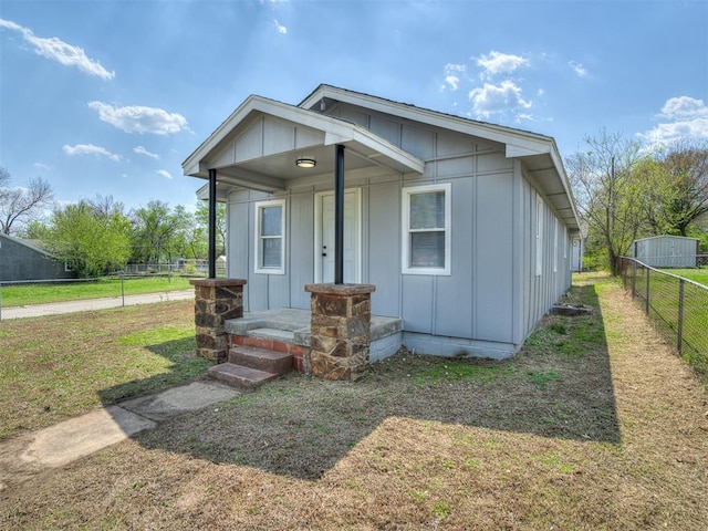 bungalow-style home with board and batten siding, a front lawn, fence, and covered porch