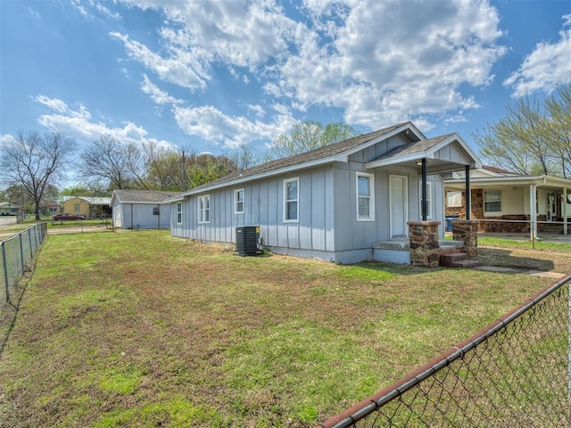 exterior space featuring central AC unit, board and batten siding, fence, and a lawn