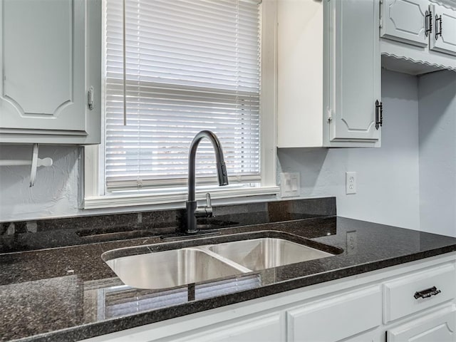 kitchen with white cabinets, a sink, and dark stone counters