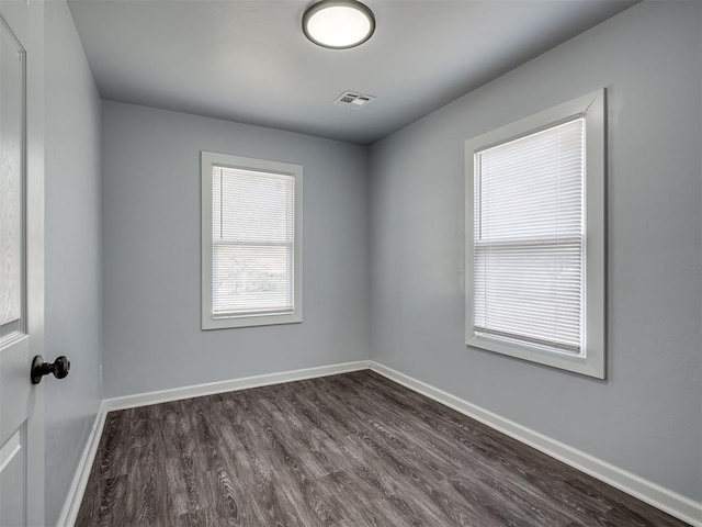 unfurnished room featuring dark wood-type flooring, visible vents, and baseboards