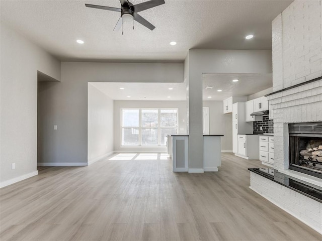 unfurnished living room with baseboards, a brick fireplace, ceiling fan, light wood-style floors, and a textured ceiling