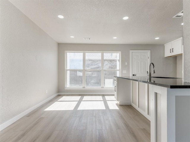 kitchen featuring baseboards, dark countertops, white cabinets, visible vents, and light wood finished floors