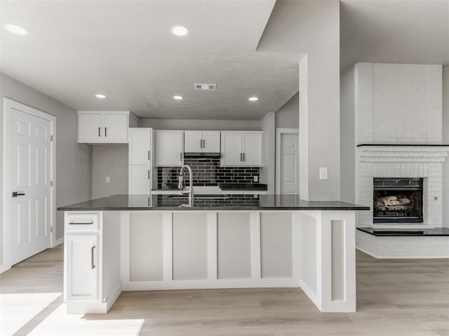 kitchen with visible vents, a fireplace, white cabinetry, light wood-style flooring, and decorative backsplash