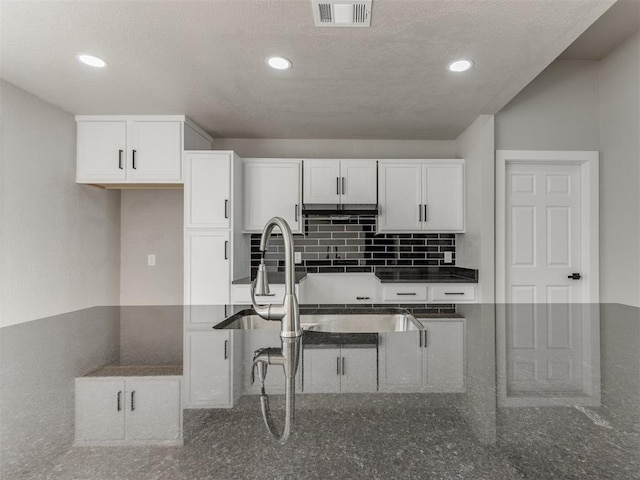 kitchen with white cabinets, visible vents, and dark stone counters