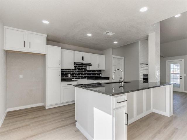 kitchen featuring dark stone countertops, a peninsula, white cabinets, under cabinet range hood, and a sink