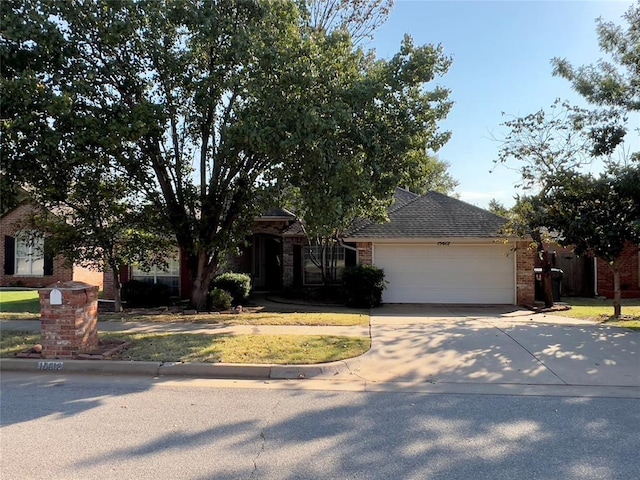 view of property hidden behind natural elements featuring an attached garage, a shingled roof, driveway, and brick siding