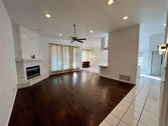 unfurnished living room featuring light wood-style floors, a ceiling fan, visible vents, recessed lighting, and a tiled fireplace