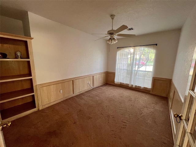 unfurnished room featuring visible vents, a wainscoted wall, a ceiling fan, and carpet floors