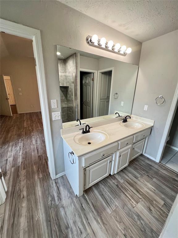 bathroom with a textured ceiling, wood finished floors, double vanity, and a sink
