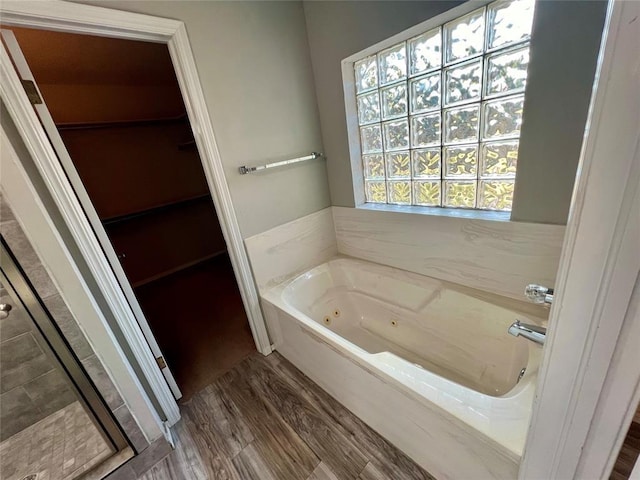 full bathroom featuring a spacious closet, a stall shower, a tub with jets, and wood finished floors