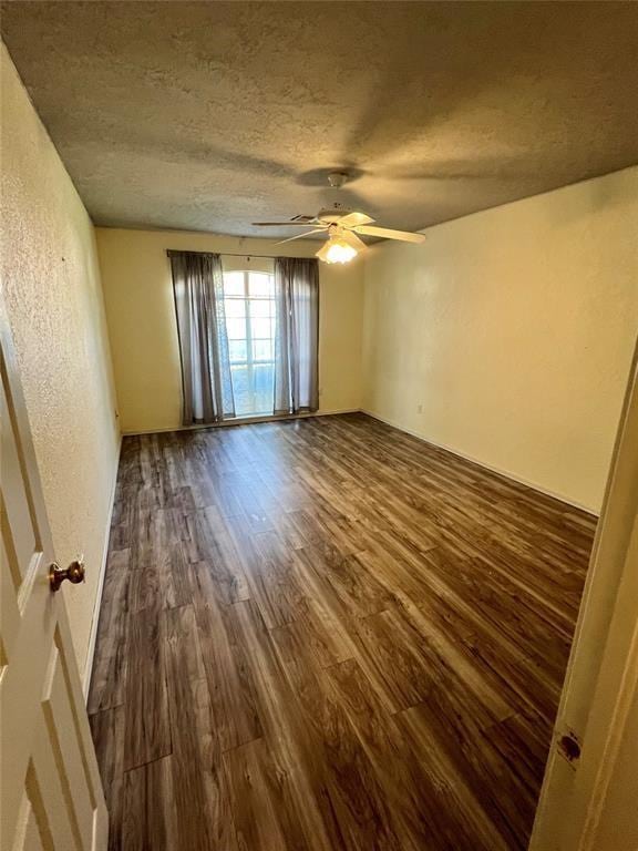 spare room featuring a textured wall, dark wood-type flooring, a textured ceiling, and ceiling fan