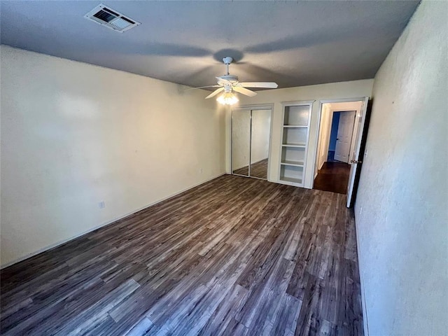 unfurnished bedroom with dark wood-style flooring, visible vents, ceiling fan, and a closet