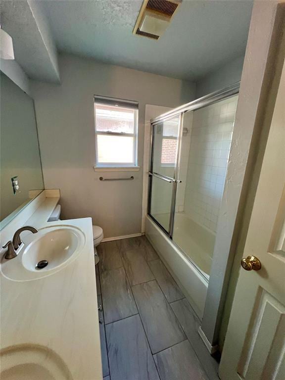 bathroom with visible vents, combined bath / shower with glass door, toilet, vanity, and marble finish floor