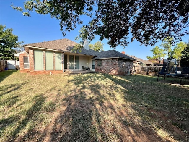 rear view of house featuring a trampoline, a fenced backyard, a yard, and brick siding