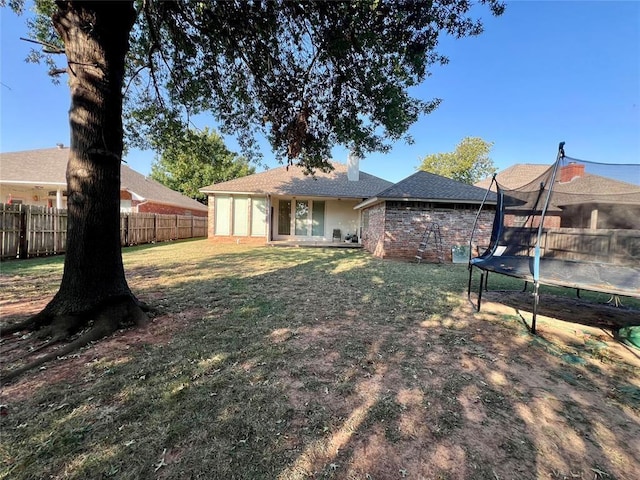 back of property with a yard, a trampoline, a chimney, a fenced backyard, and brick siding