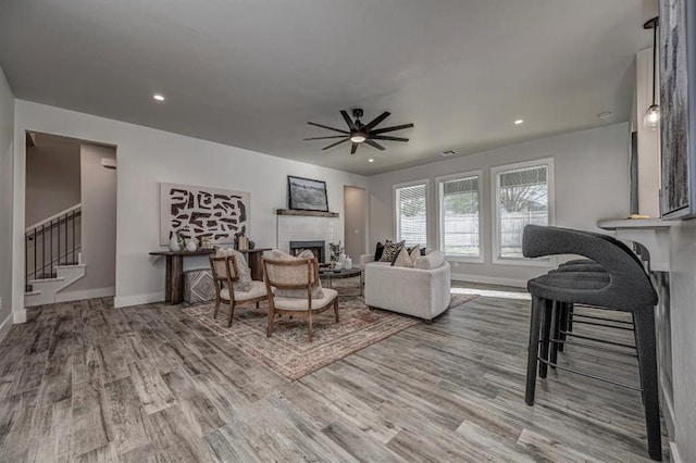 living area with a fireplace, stairway, baseboards, and a ceiling fan