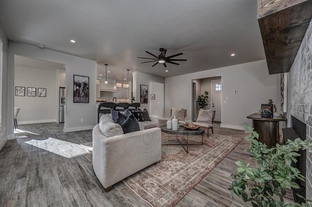 living area featuring ceiling fan, baseboards, dark wood finished floors, and a fireplace