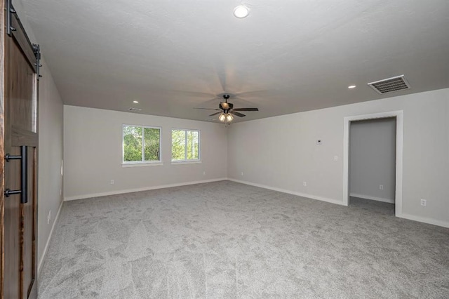 unfurnished room featuring carpet flooring, a ceiling fan, visible vents, and a barn door