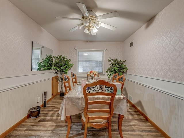 209 S 2nd Ave, Stroud, OK 74079 - dining space featuring visible vents, a ceiling fan, wainscoting, wood finished floors, and wallpapered walls