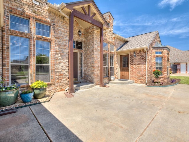 entrance to property featuring brick siding, a shingled roof, a patio area, and stone siding