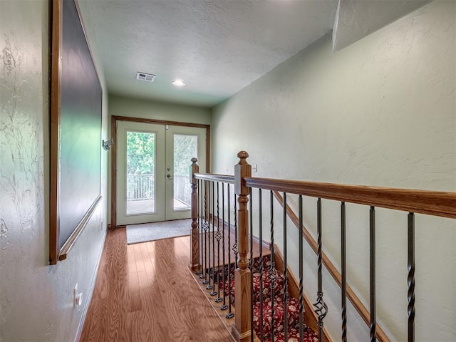 interior space featuring a textured wall, a textured ceiling, french doors, wood finished floors, and visible vents