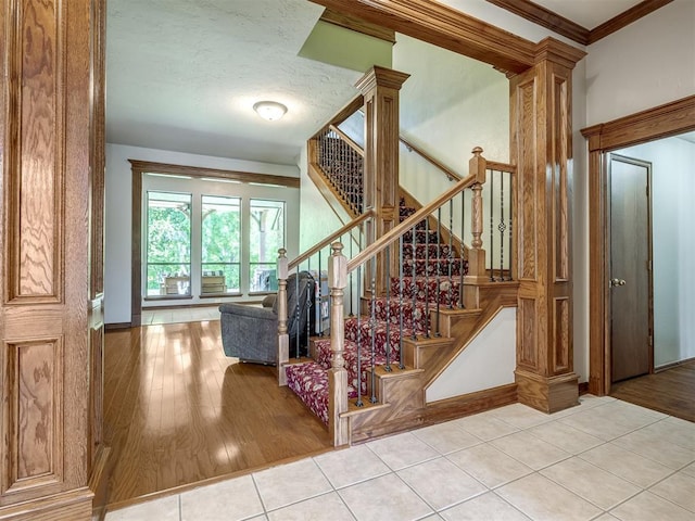 staircase with tile patterned flooring, baseboards, crown molding, and decorative columns