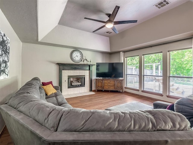 living area featuring a ceiling fan, a tile fireplace, wood finished floors, and visible vents
