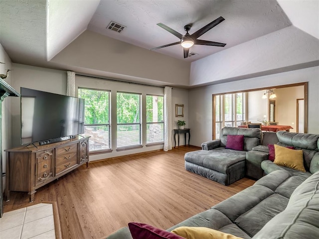 living area featuring a raised ceiling, ceiling fan, light wood-type flooring, and visible vents
