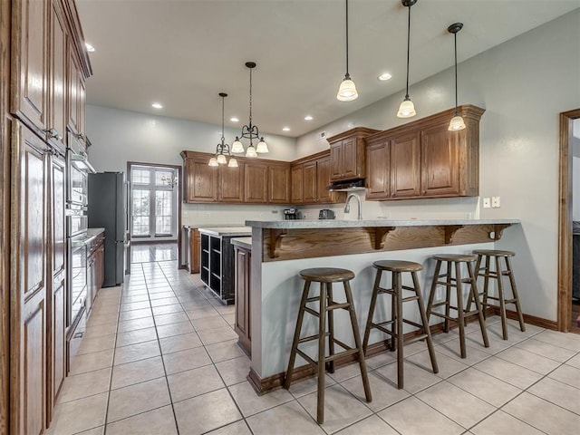 kitchen with brown cabinets, light tile patterned flooring, a breakfast bar area, a peninsula, and recessed lighting