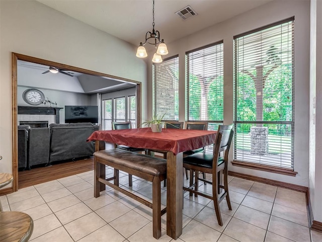 dining space with light tile patterned flooring, visible vents, ceiling fan with notable chandelier, and a tile fireplace