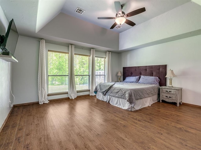 bedroom with visible vents, baseboards, wood finished floors, and a tray ceiling