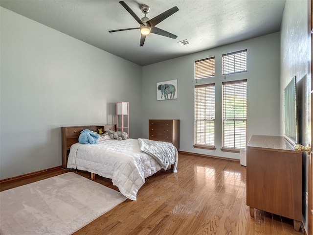 bedroom with light wood-style floors, baseboards, ceiling fan, and visible vents