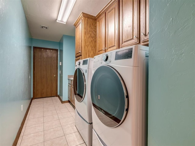 washroom with cabinet space, a textured wall, light tile patterned floors, visible vents, and washing machine and dryer