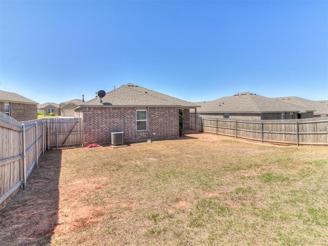 9704 Saddle Dr, Yukon, OK 73099 - rear view of house featuring a yard, a fenced backyard, brick siding, a shingled roof, and central AC unit