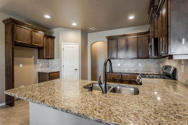 5800 SE 142nd St, Oklahoma City, OK 73165 - kitchen with gas stove, light stone counters, a peninsula, arched walkways, and a sink