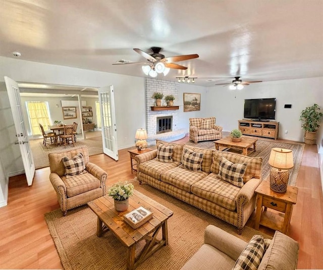 living room featuring light wood-style flooring, a ceiling fan, a brick fireplace, french doors, and baseboards