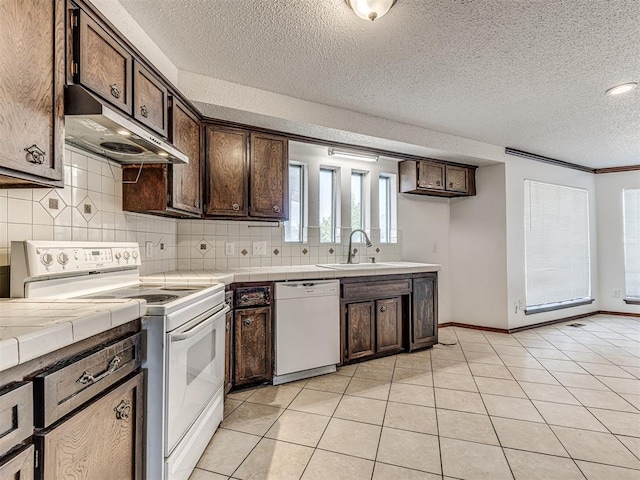 7700 S Country Club Dr, Oklahoma City, OK 73159 - kitchen featuring dark brown cabinetry, under cabinet range hood, tile counters, and white appliances